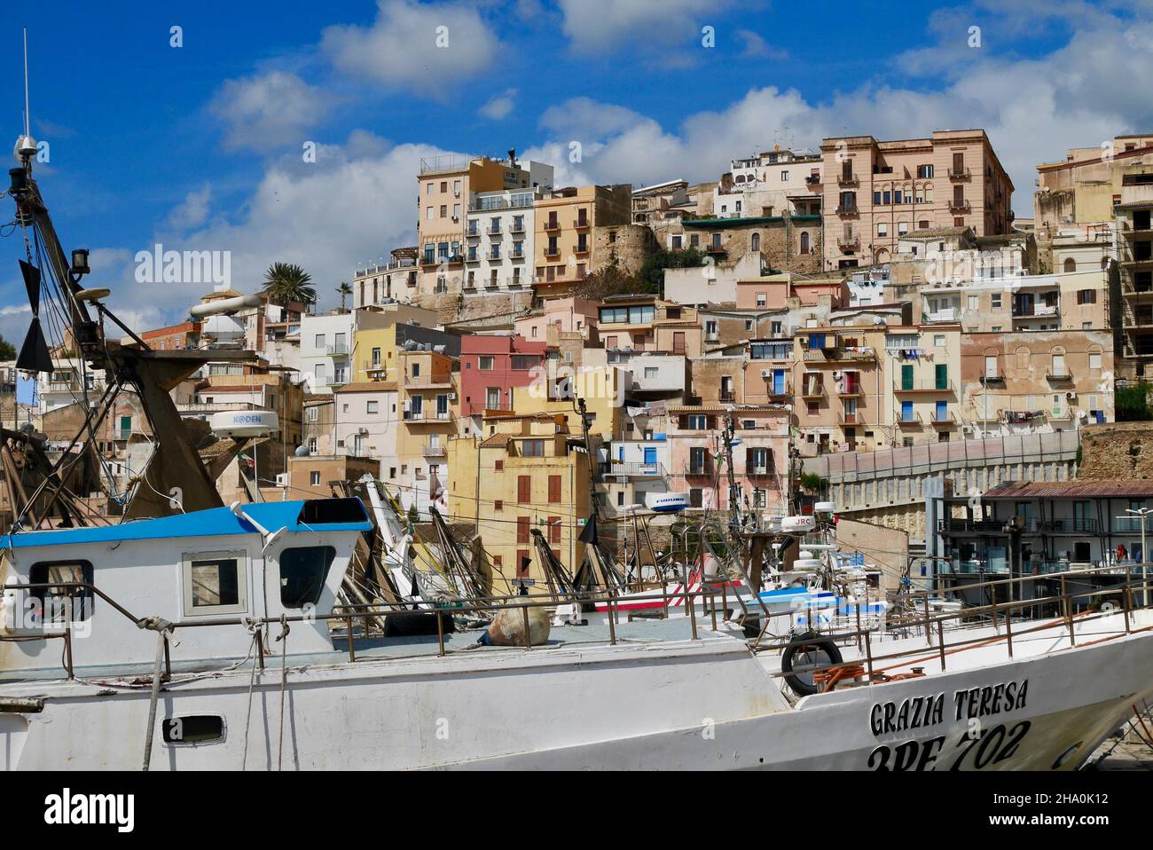 Sciacca, Sicilia, Italia, 24.03.2018. Barche da pesca nel porto con case colorate della città vecchia sullo sfondo. Foto Stock