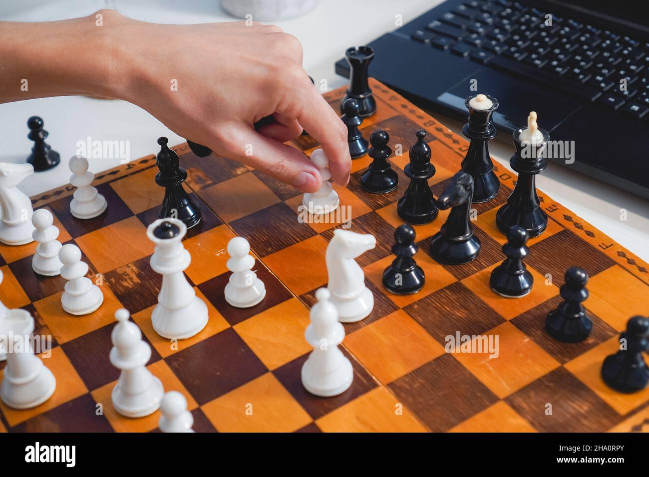 L'uomo gioca a scacchi su tavola di legno vicino a un computer portatile. Vista dall'alto. Messa a fuoco selettiva. Strategia e concetto di concorrenza Foto Stock