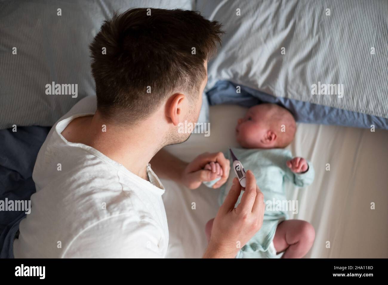 Preoccupato il padre di un'unga che guarda il termometro che tiene il suo neonato nelle mani. Foto Stock