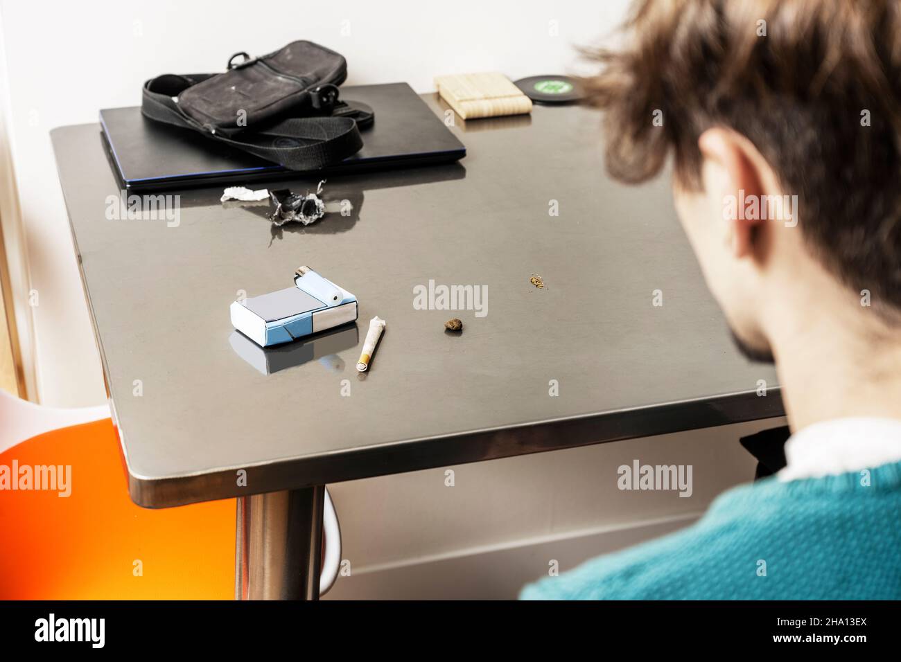 Giovane uomo che guarda la sua sigaretta ridente su un tavolo di metallo grigio Foto Stock