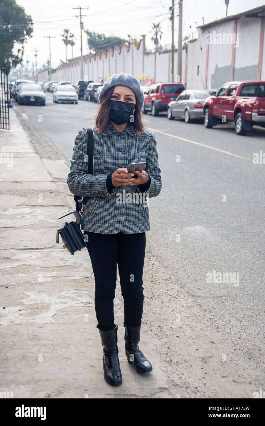 Cristina Sandoval, residente di Tijuana Messico di 46 anni, si trova sul marciapiede di una strada a Tijuana, Messico, con una maschera. Foto Stock