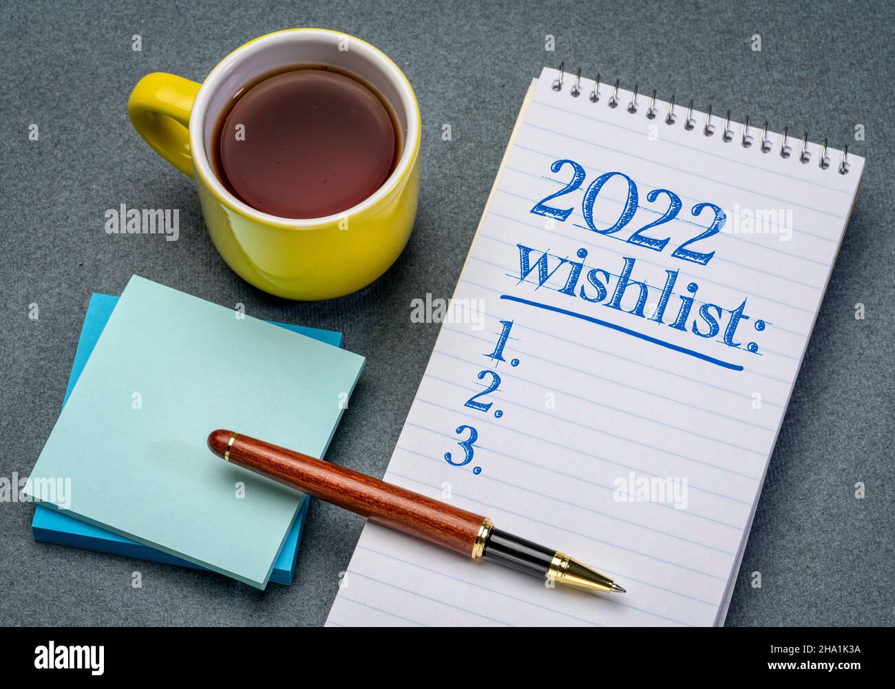2022 wishlist - scrittura a mano in un taccuino a spirale con una tazza di tè, speranze e aspettative per il nuovo anno Foto Stock