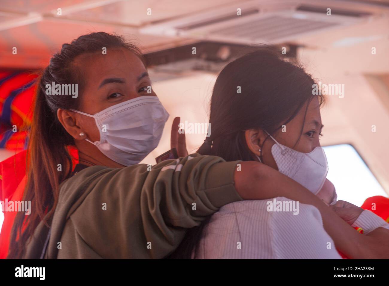 2 donne, turisti nazionali, (1 cambogiani, a sinistra, 1 razza mista, Destra, 1/4 vietnamita, 1/4 Cham, 1/4 cinese e 1/4 cambogiano), indossando maschere protettive per il viso, fare un giro in traghetto per Saracen Bay, Koh Rong Samloem durante il COVID - 19 pandemia. Provincia di Sihanoukville, Cambogia. 6th dicembre 2021. © Kraig Lieb Foto Stock