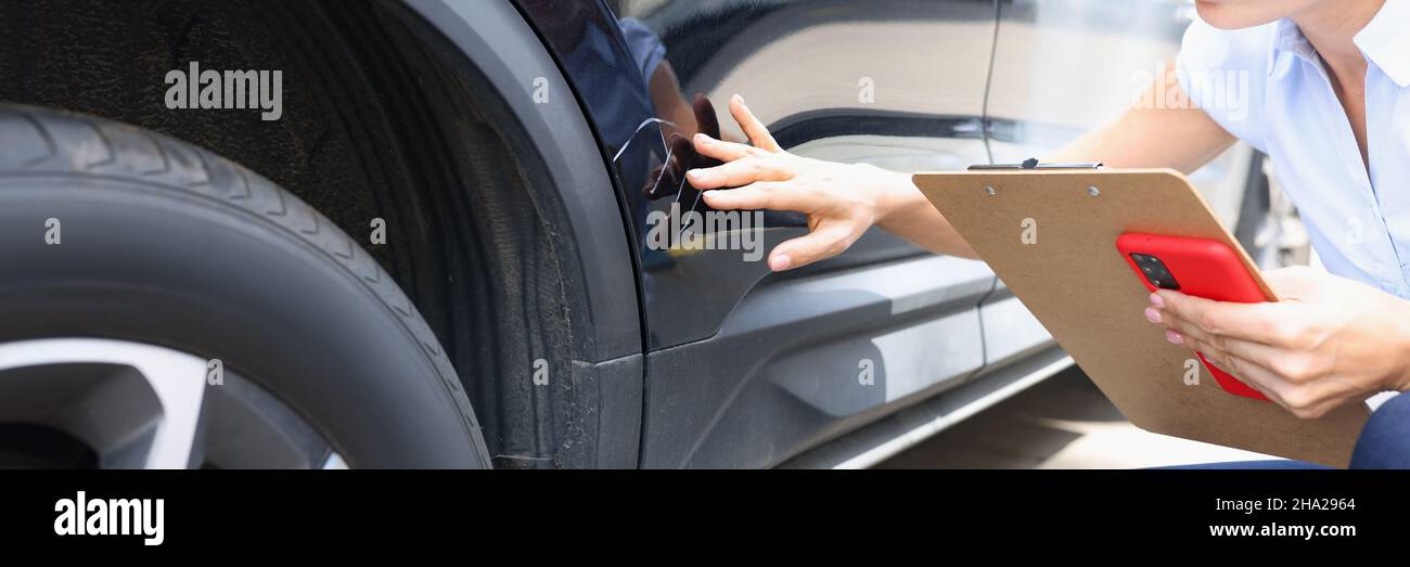 Agente assicurativo che compila il modulo assicurativo in prossimità di auto nera danneggiata Foto Stock