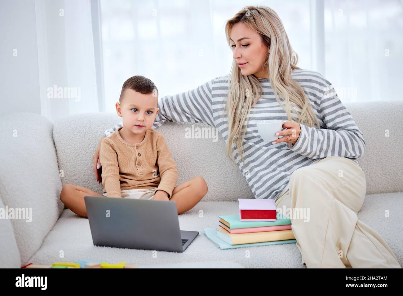 mamma carina che si rilassa sul comodo divano con un piccolo figlio in età prescolare, guardando i video sul portatile. Attraente felice madre che mostra l'applicazione educativa t Foto Stock