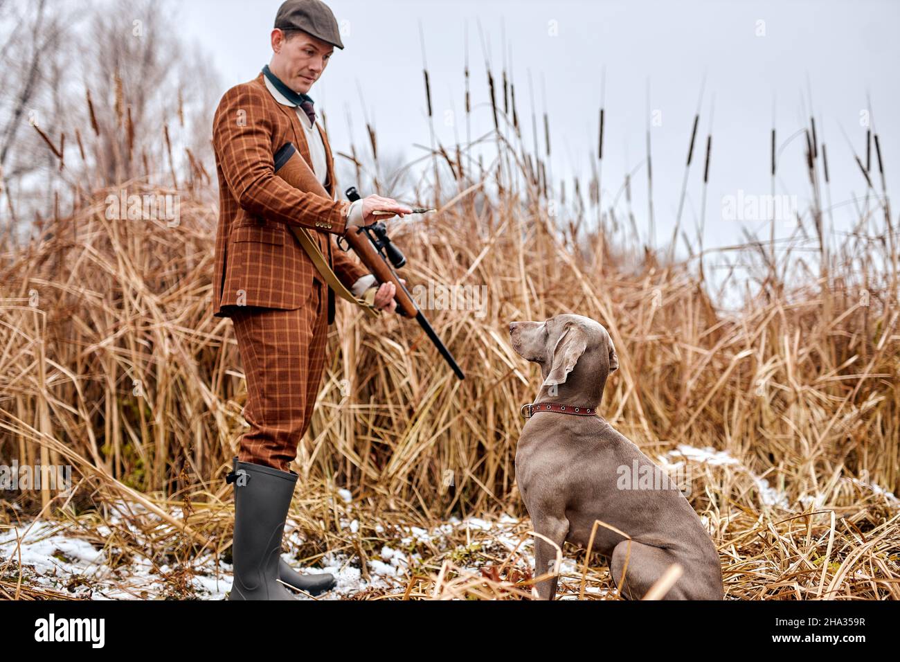 stagione autunnale di caccia aperta. maschio caucasico in tuta marrone, cacciatore o poacher dare comandi, addestrare il cane prima di caccia. stile di vita attivo, l'uomo parlare Foto Stock