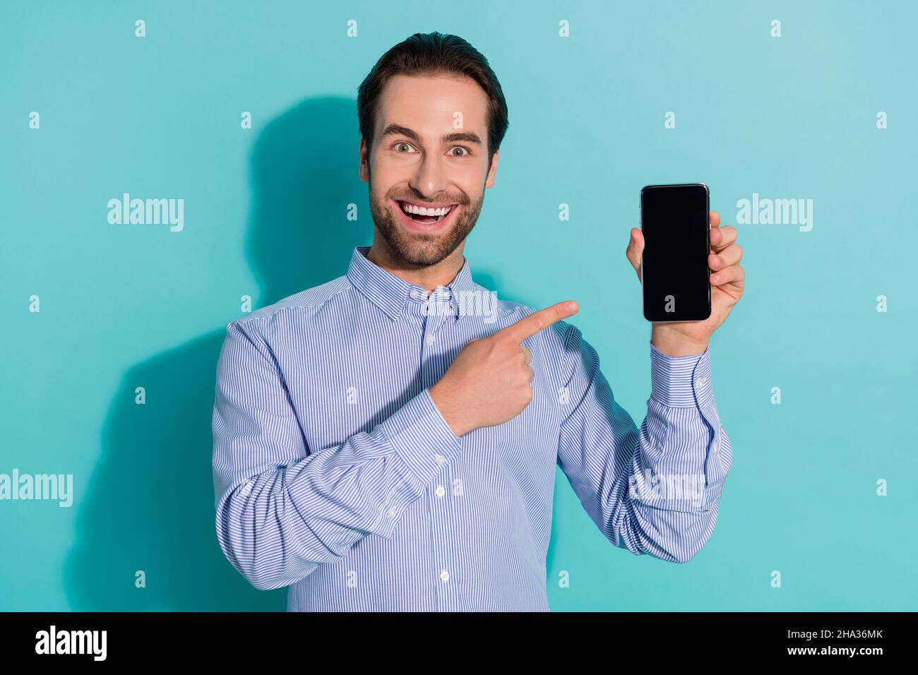 Foto di ragazzo eccitato indicare indice telefono schermo spazio vuoto indossare camicia viola isolato colore teal sfondo Foto Stock