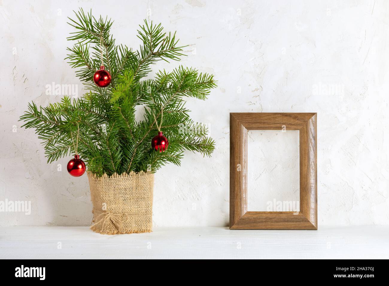 Immagine minimale di Natale alla moda con bouquet di rami di abete come alternativa albero di Natale e cornice di legno vuota per foto su sfondo bianco. Decorazione di festa Foto Stock