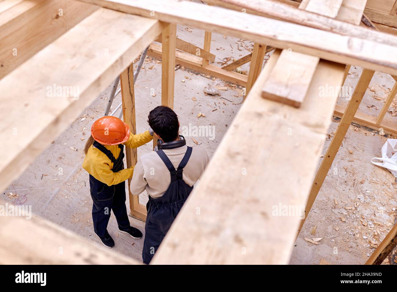 Vista dall'alto su due architetti ingegneri costruttori che lavorano insieme, costruzione casa cottage in legno. I carpentieri giovani che lavorano duro in abiti speciali lavorano un Foto Stock
