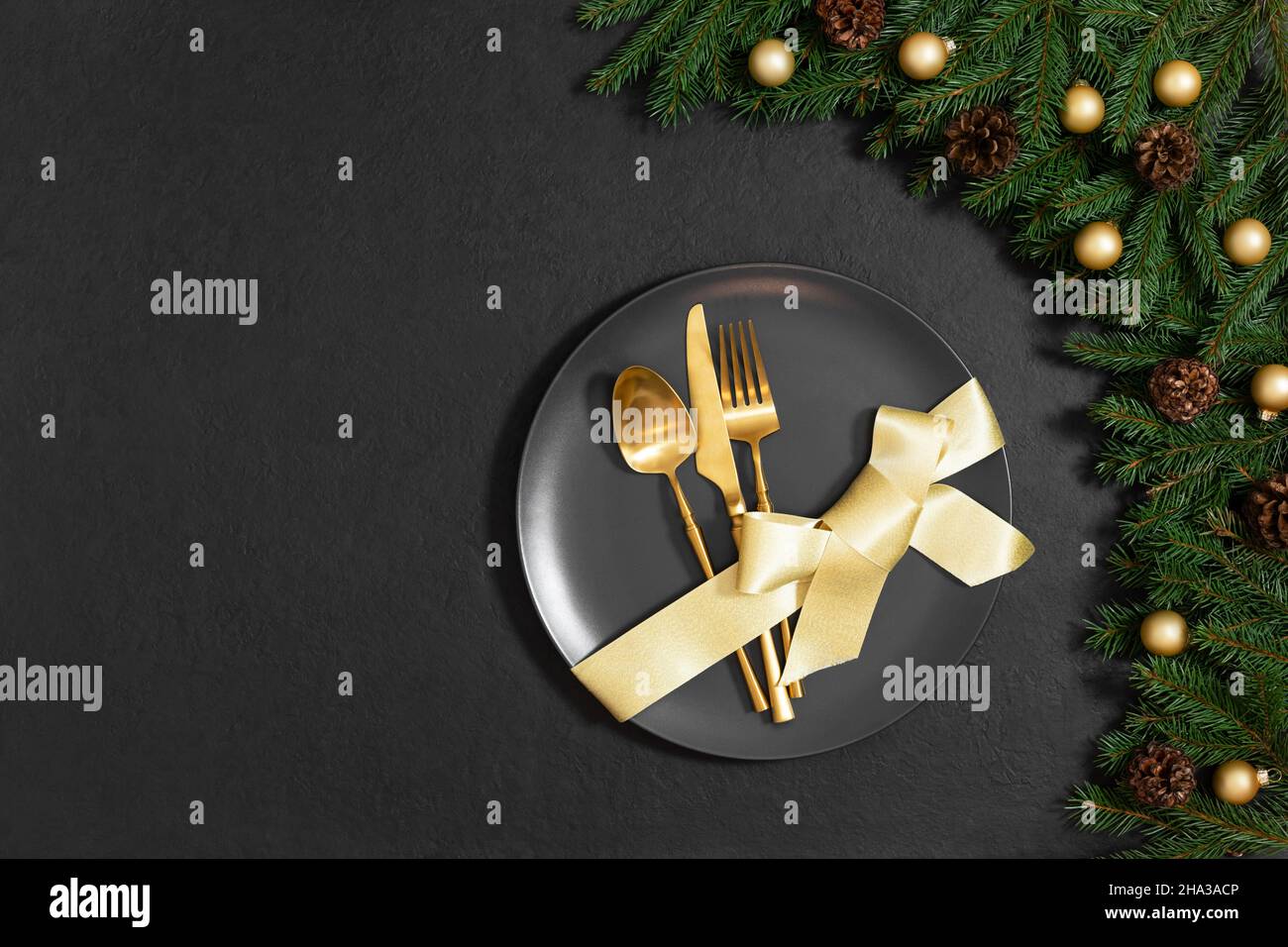 Tavolo di Natale con posate d'oro e arco in un piatto su sfondo nero. Felice Anno Nuovo. Spazio per il testo. Vista dall'alto, piatto. Foto Stock