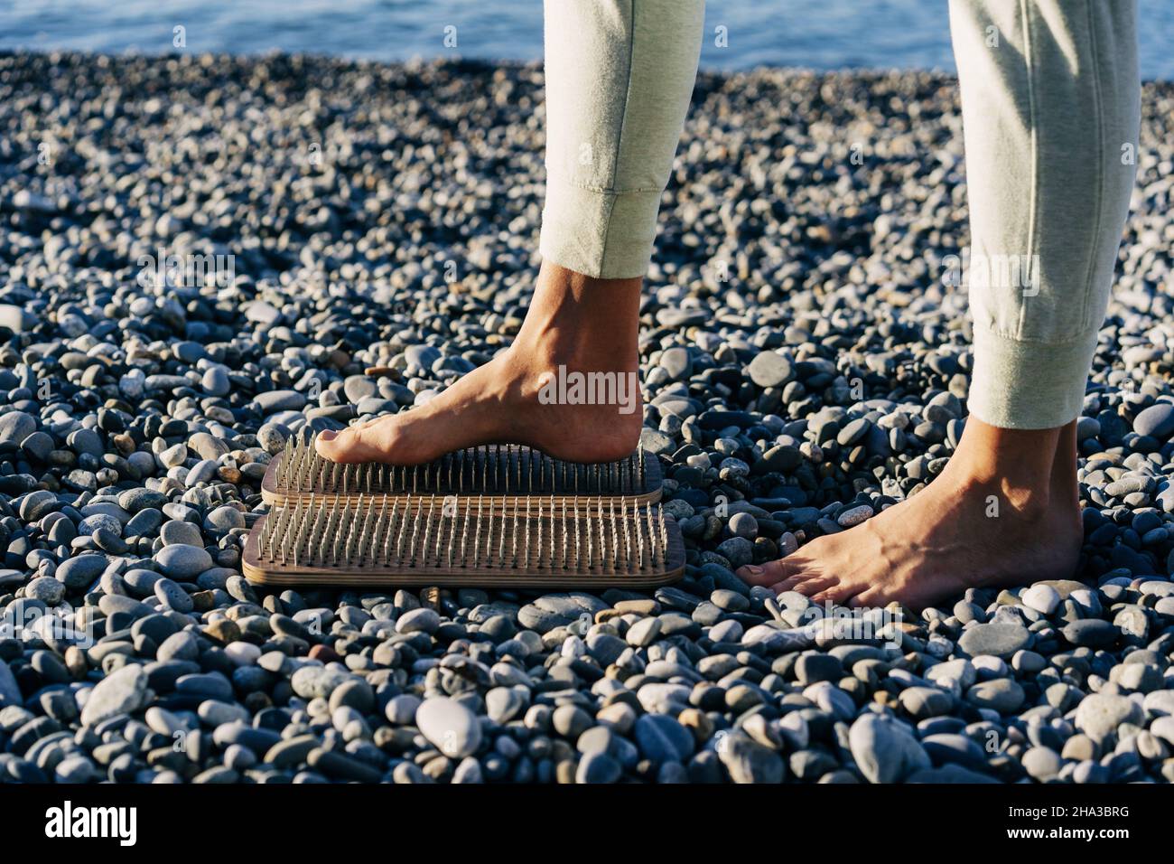 Il piede femminile a piedi nudi si trova su un asse di legno con chiodi per la pratica della concentrazione a riva Foto Stock