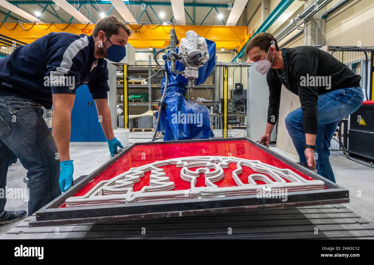 10 dicembre 2021, Sassonia, Chemnitz: Enrico Rudolph (r), responsabile del gruppo di lavoro "Additive Lightweight Technologies" presso il dipartimento di ricerca "Lightweight Structures in Civil Engineering" dell'Università di tecnologia Chemnitz, e l'assistente di ricerca Daniel Schönfelder trasportano una lastra con un flybow in calcestruzzo stampato a 3D. Gli scienziati dell'Institute for Lightweight Structures presso la Chemnitz University of Technology ricercano tecnologie automatizzate di produzione di additivi per cinque anni. Recentemente, hanno presentato il primo contrafforte volante in calcestruzzo stampato a 3D° del mondo. Una fibra speciale- Foto Stock