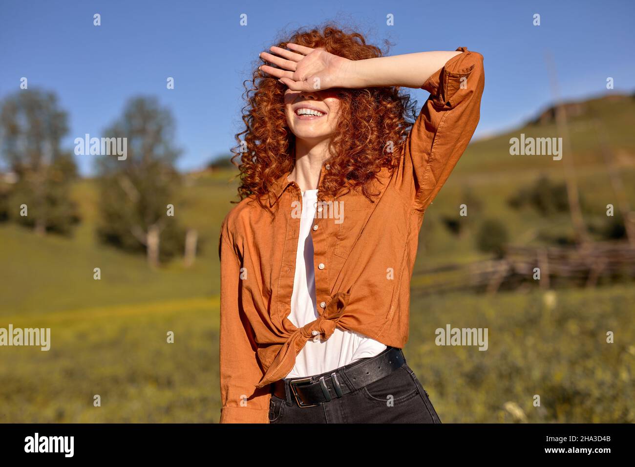 cute redhead signora nasconde il viso dal sole la sera in natura, foresta sullo sfondo. ritratto di buon aspetto felice sorridente femmina in casual oran Foto Stock