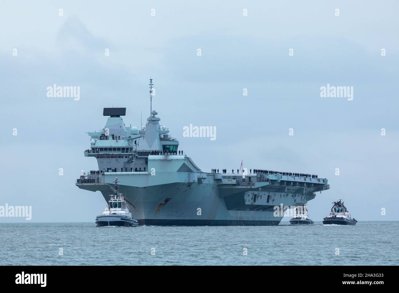 2021 dicembre, HMS Queen Elizabeth arrivo nel Solent. L'equipaggio è alla procedura alpha che fiancheggiano il ponte. Accompagnato al porto da rimorchiatori SERCO Foto Stock