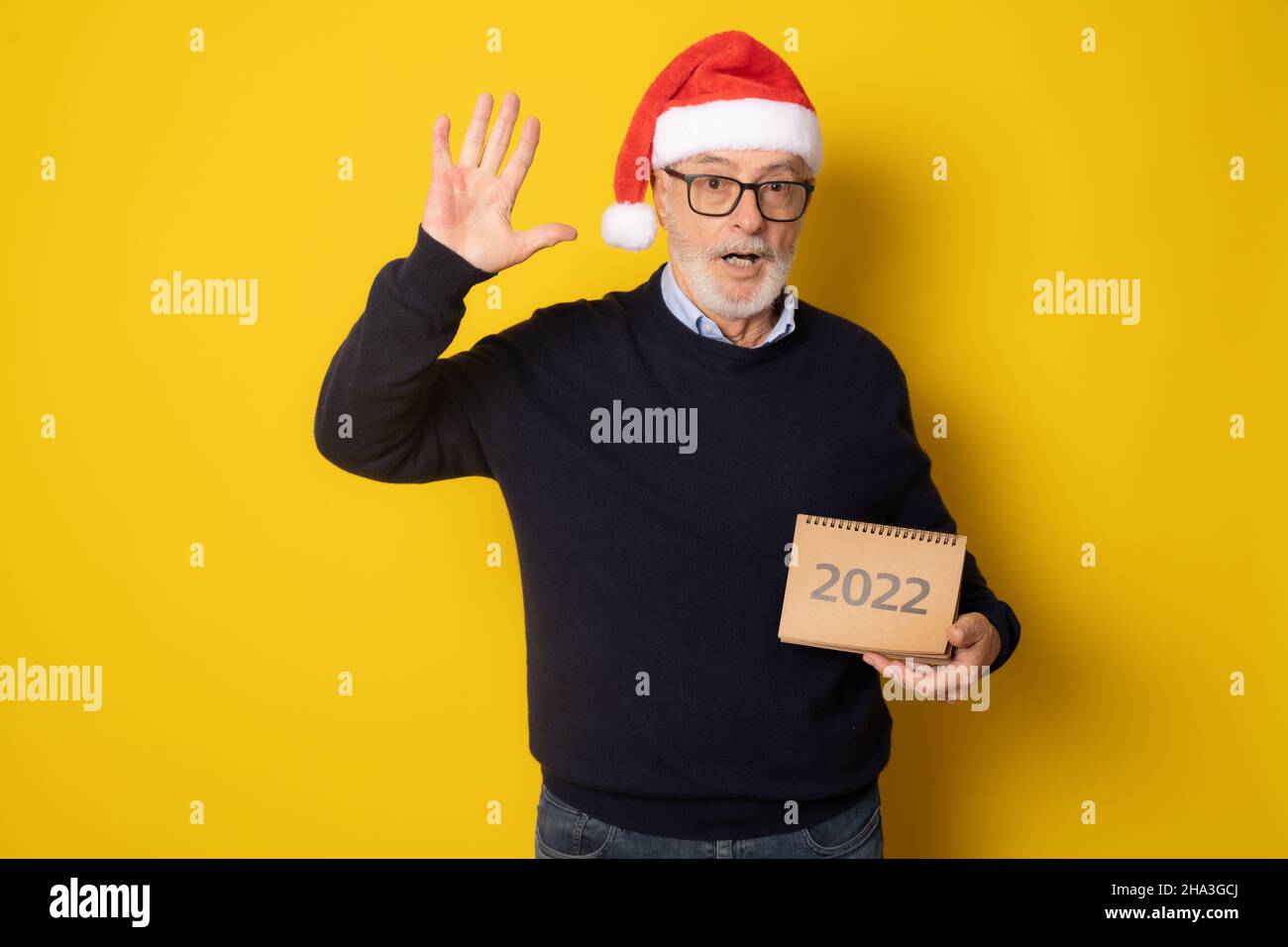 Uomo eccitato senior indossando santa cappello mostrando calendario isolato su sfondo giallo. Foto Stock