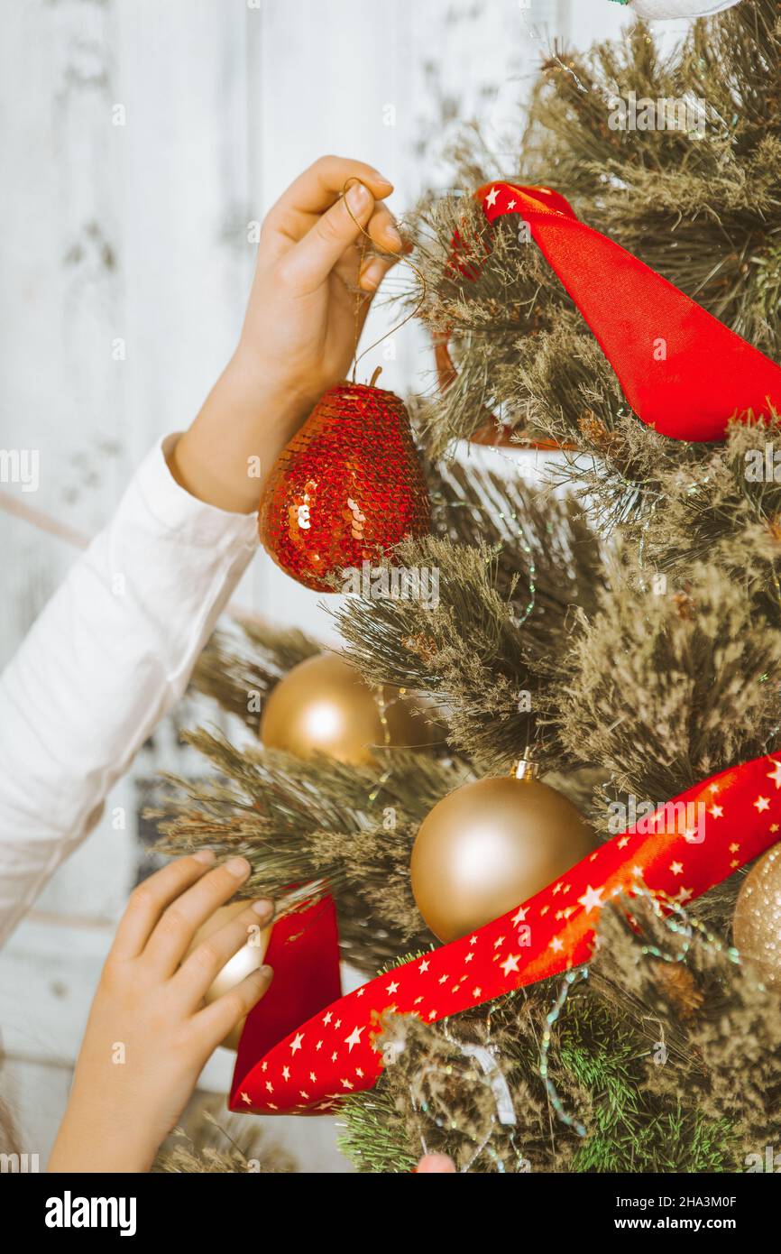 Le mani dei bambini appendono una sfera rossa decorativa su un ramo di un albero di Capodanno. Capodanno, mezzanotte. Primo piano. Foto di alta qualità Foto Stock