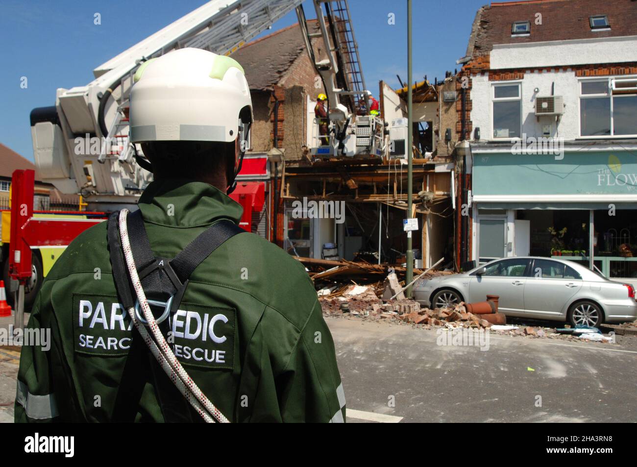 A Paramedic effettua un'indagine su un edificio danneggiato a seguito di un'esplosione mentre i pompieri lavorano nei detriti. Foto Stock