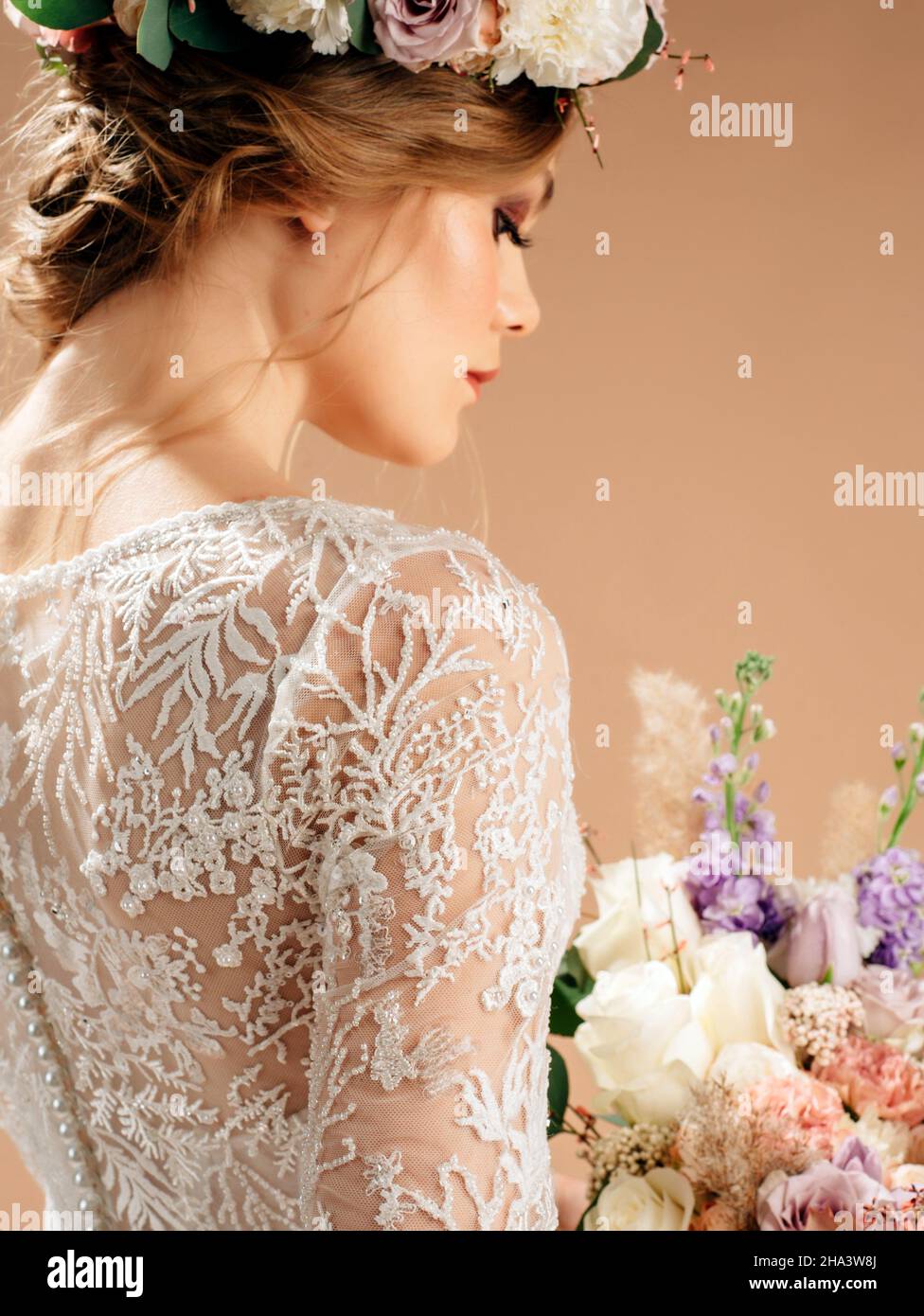 Bella sposa in una corona floreale con bouquet nuziale. Primo piano ritratto in studio con sfondo pesca. Foto Stock