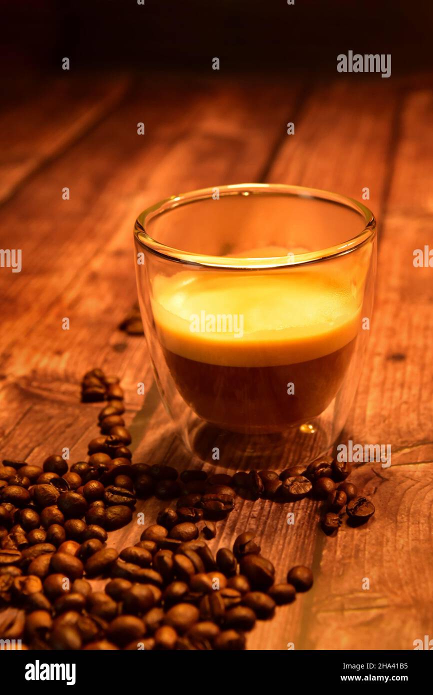 Vista frontale di una tazza di vetro di delizioso caffè su un rustico tavolo in legno con chicchi di caffè. Foto Stock