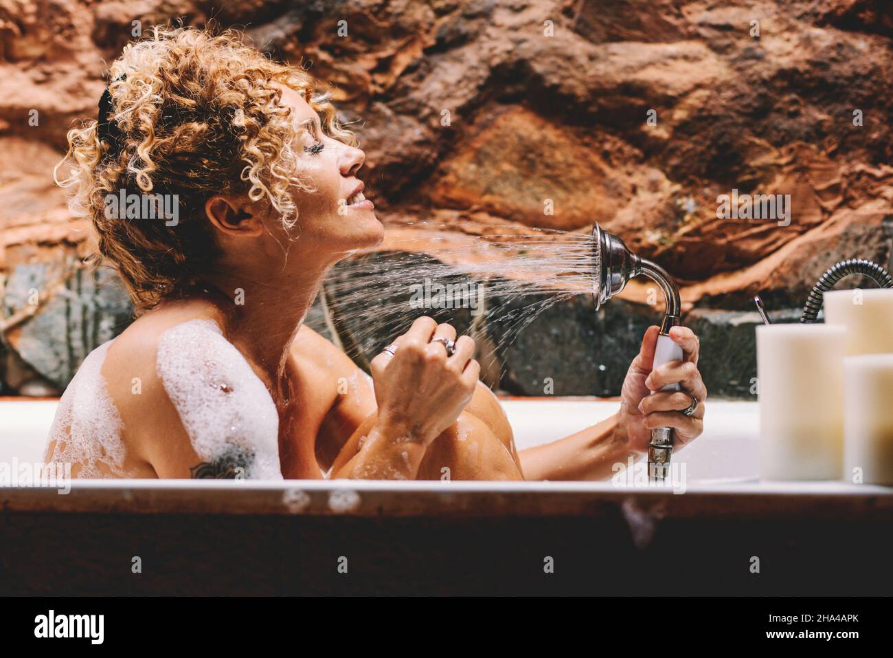 felice bella giovane donna adulta lavaggio con doccia seduta in bagno a casa. cura del corpo e bellezza fanno più lifestyle femminile persone godere di sapone e acqua in bagno Foto Stock