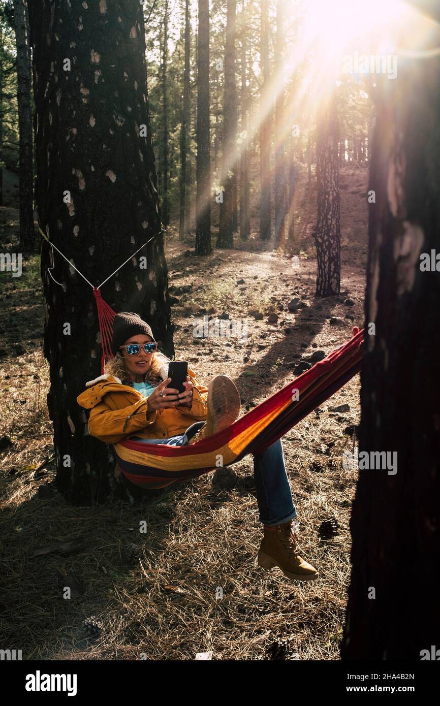 la donna caucasica del medio evo ha una chiamata telefonica nel parco naturale esterno adagiarsi su amaca fra gli alti alberi - concetto di dappertutto la gente di collegamento con la tecnologia di roaming Foto Stock