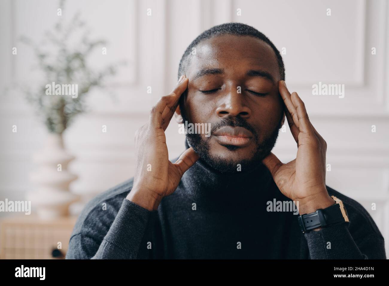 Stressato lavoratore di casa africano si siede alla scrivania toccando templi mentre gli occhi chiusi Foto Stock