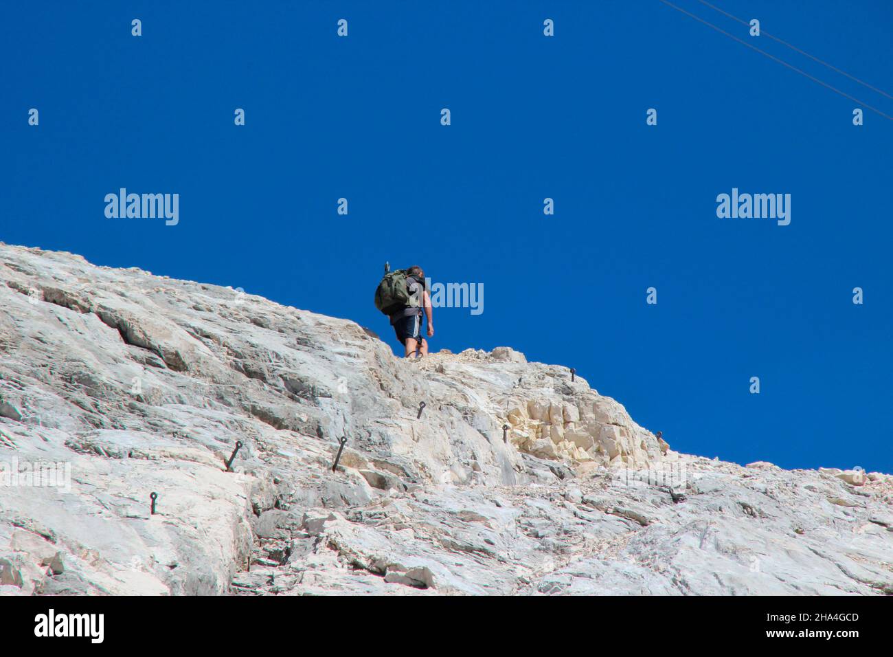uomo di mezza età sulla via ferrata a zugspitze, vista dal basso, wetterstein montagne blu cielo, zaino, garmisch-partenkirchen, loisachtal, alta baviera, baviera, germania meridionale, germania, europa, Foto Stock