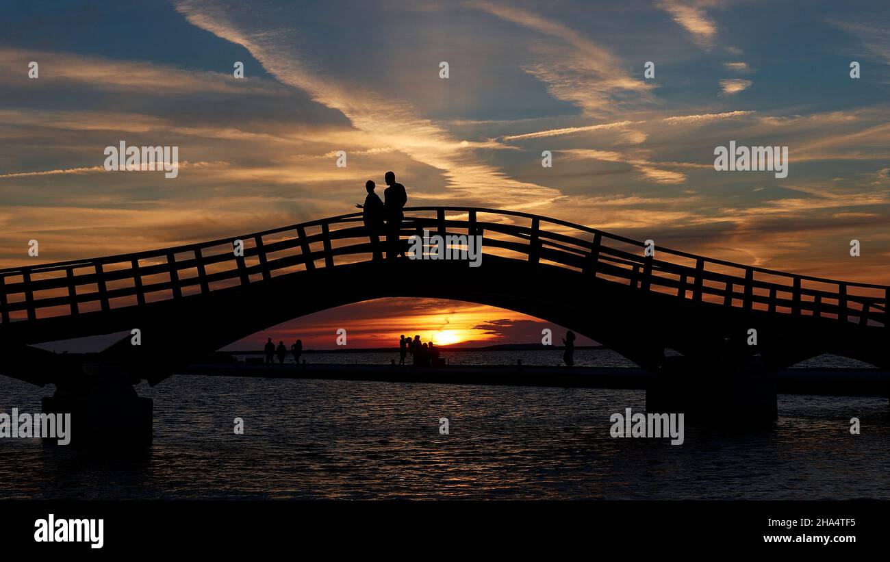 grecia,isole greche,isole ionie,lefkada o lefkas,lefkada city,capitale,crepuscolo,atmosfera serale,tramonto,sezione centrale del ponte di legno,su di esso una coppia come silhouette,il sole scende sotto il ponte,cielo sopra il blu scuro con nuvole grigio-bianche Foto Stock