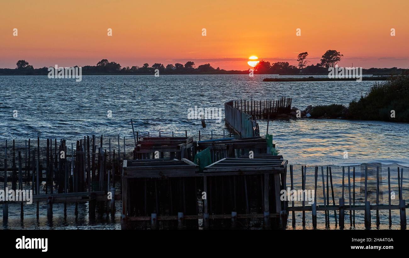 grecia,isole greche,isole ionie,lefkada o lefkas,lefkada city,capitale,crepuscolo,atmosfera serale,tramonto,trappole di pesce in primo piano,fila di alberi con il sole sullo sfondo,cielo arancione Foto Stock