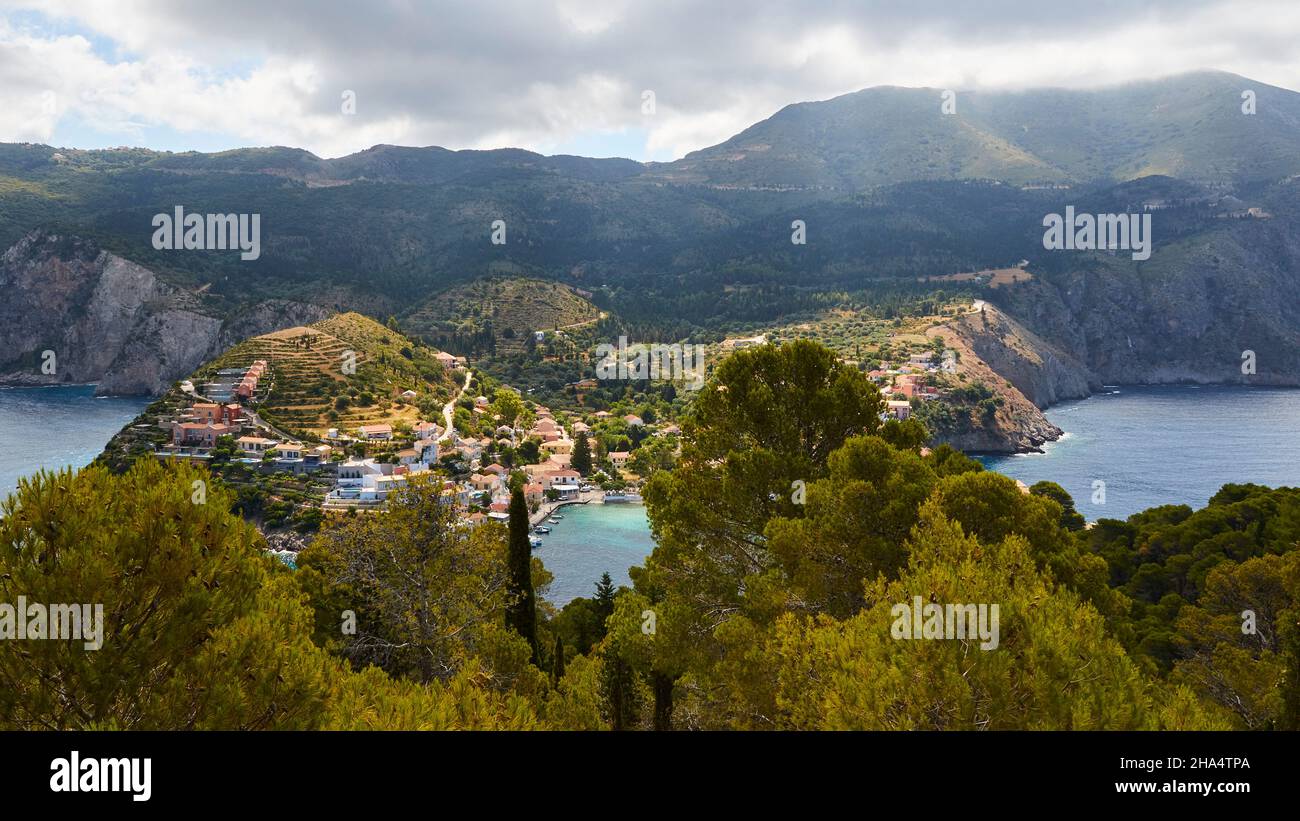 grecia,isole greche,isole ionie,cefalonia,assos,posto sulla costa occidentale,fortezza veneziana,vista dalla fortezza fino ad assos,cielo nuvoloso,montagne sullo sfondo,asso illuminato dal sole,foresta in primo piano Foto Stock