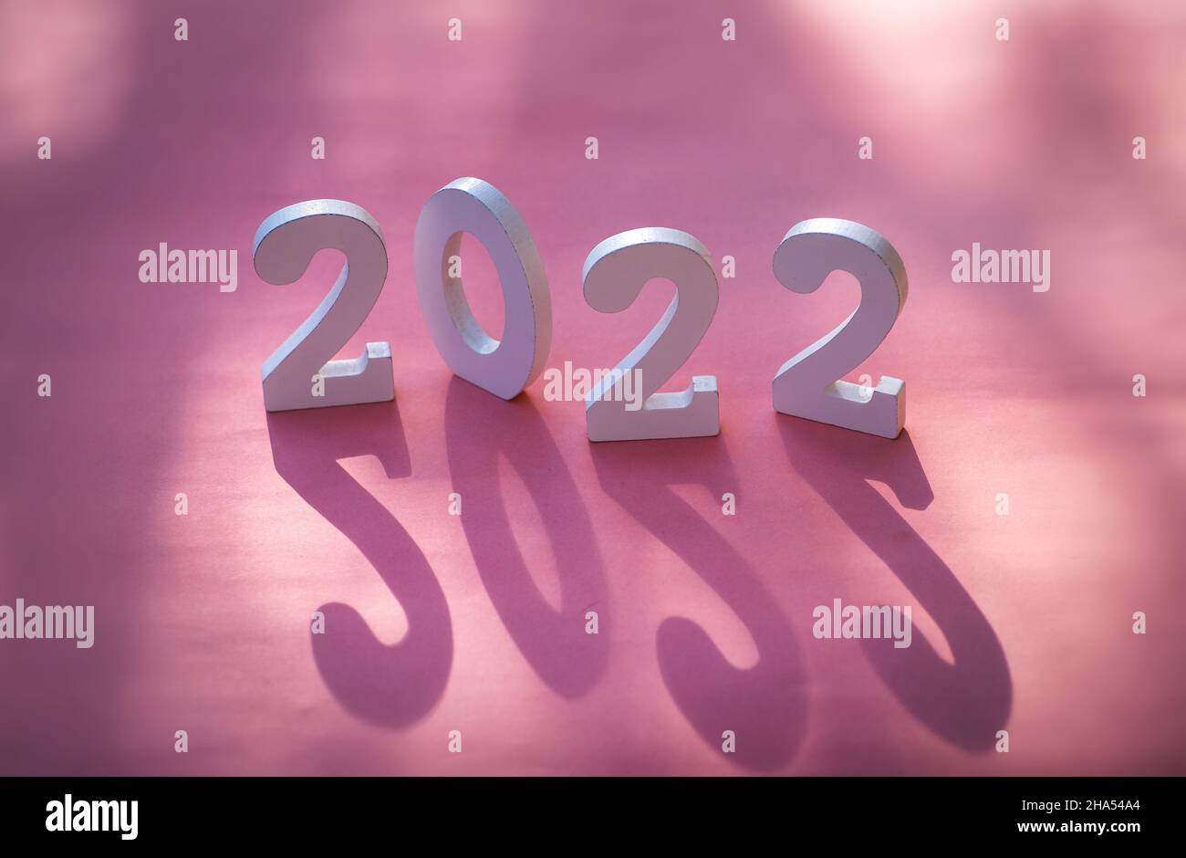 Cartello di Capodanno 2022 in legno su sfondo festivo con spazio copia su sfondo rosa con forte ombra per creare profondità Foto Stock