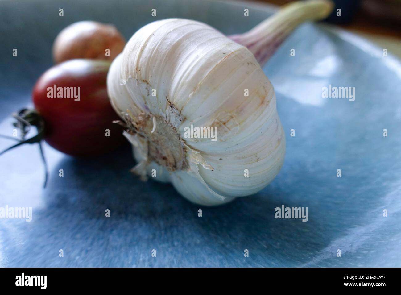 bulbo d'aglio su un piatto blu. ci sono verdure sullo sfondo. Foto Stock