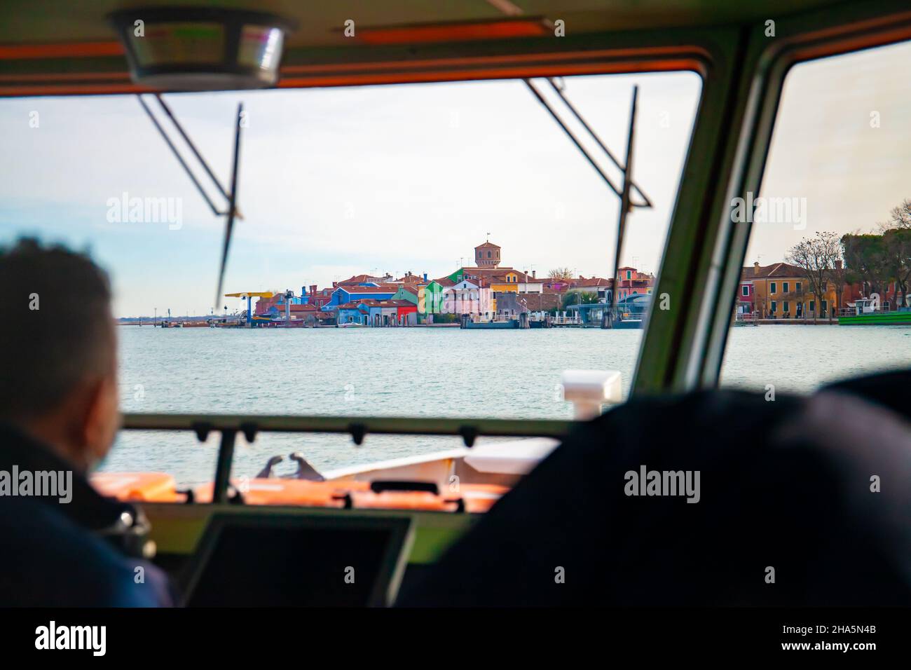 Venezia. Italia. L'isola di Burano con le sue case colorate è visibile dall'interno di un pozzetto di un traghetto con il capitano che la pilota. Vaporetto Foto Stock