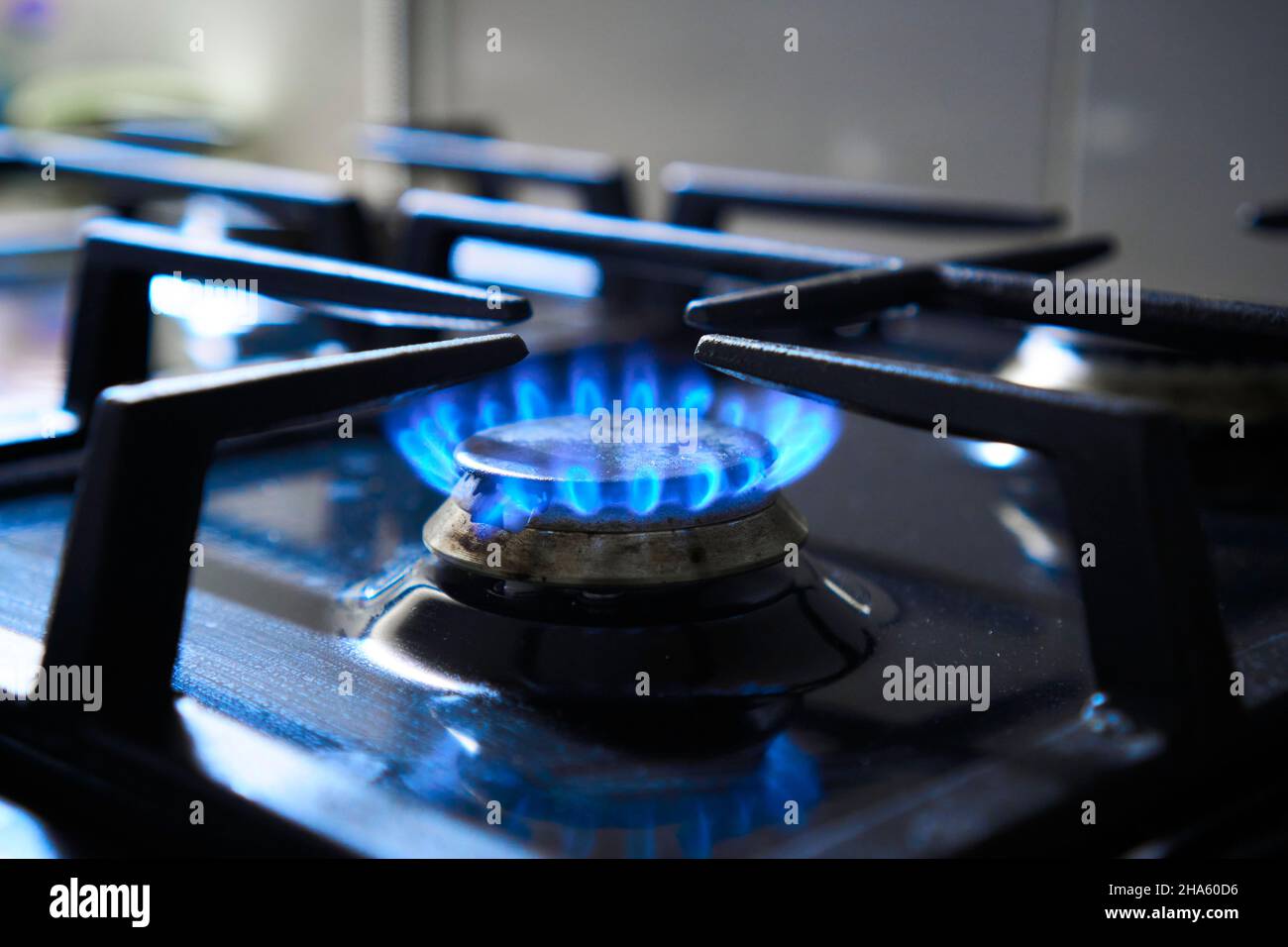 La fiamma blu del piano cottura a gas produce emissioni di gas serra. Grata di stufa da cucina su un bruciatore alimentato da gas naturale combustibile o syngas, propano Foto Stock
