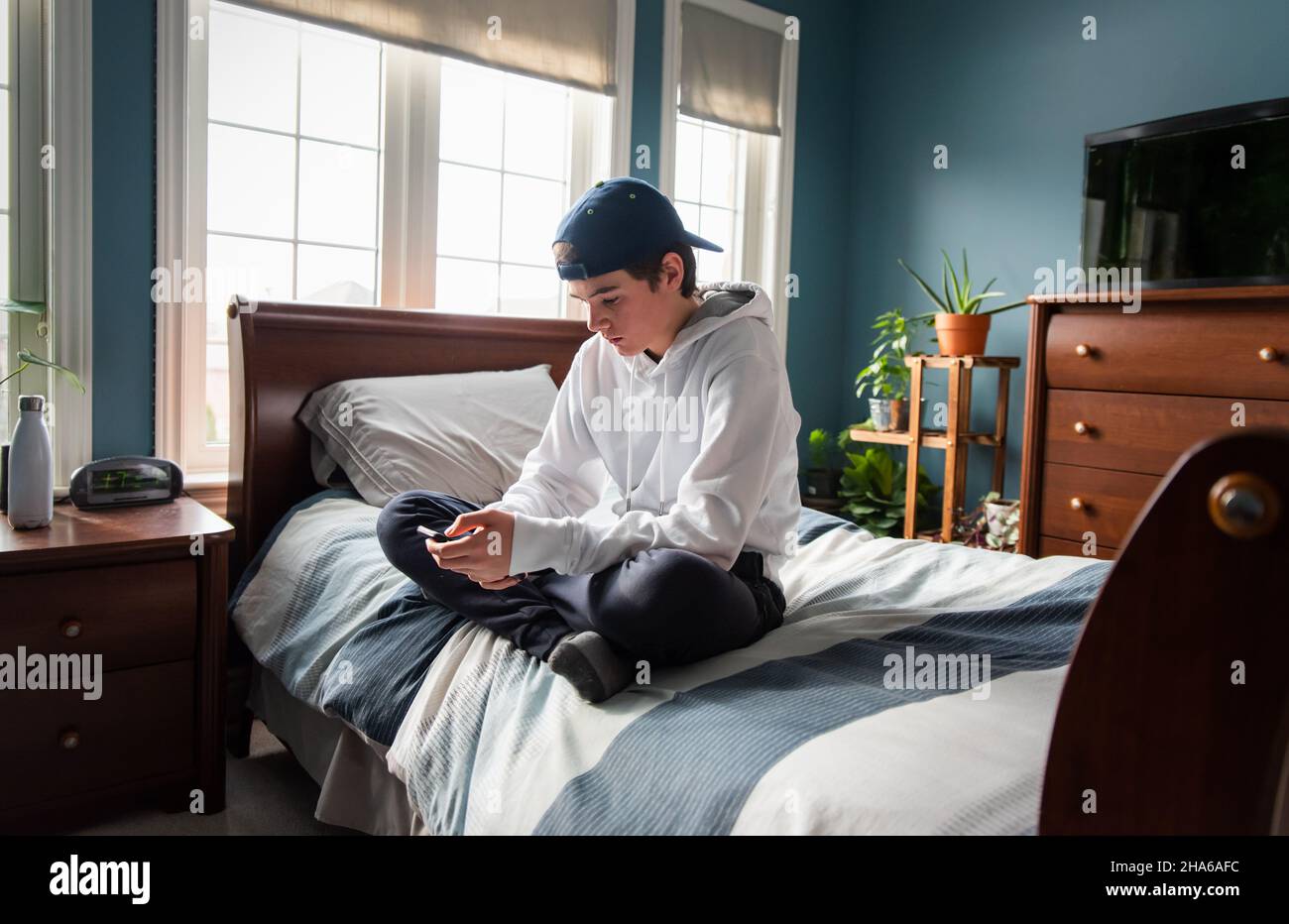 Ragazzo in felpa bianca con cappuccio su smartphone da solo nella sua camera da letto. Foto Stock
