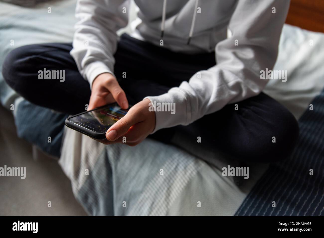 Primo piano di mani di ragazzo teen in maglione bianco SMS sul telefono. Foto Stock