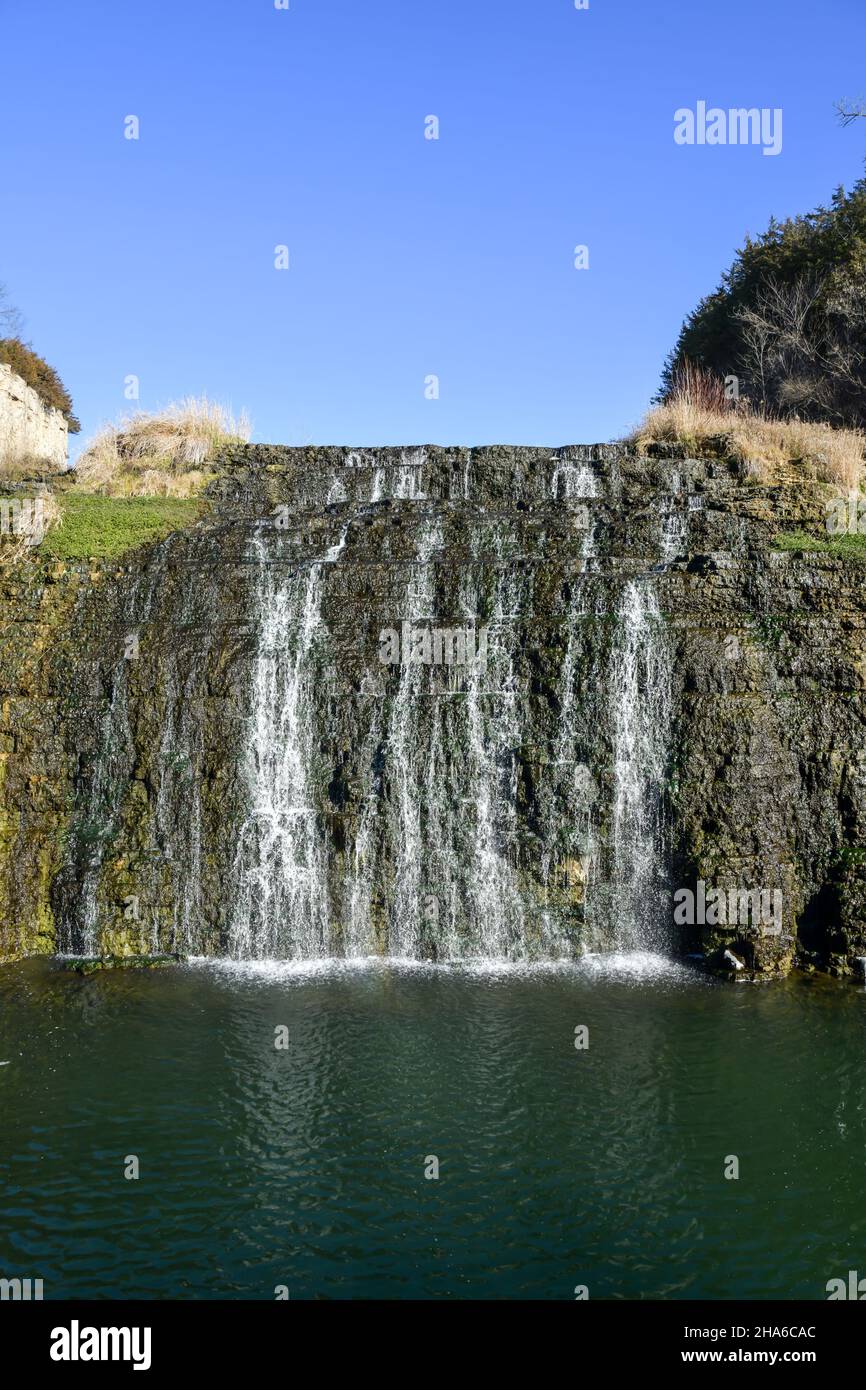 Cascata che scheggia sul bordo roccioso del lago sotto il cielo blu Foto Stock