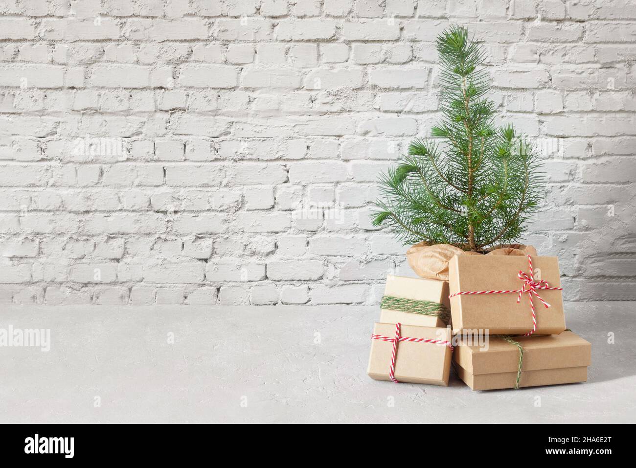 Piccolo albero di Capodanno con scatole regalo di Natale sullo sfondo muro di mattoni, concetto di zero rifiuti Foto Stock