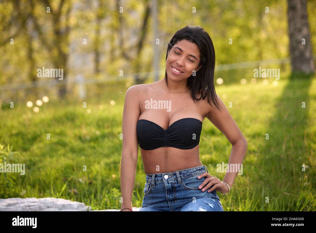 Donna colombiana sorridente in piedi con la maglia nera e jeans sotto la calda luce del sole in un parco di Toronto, Ontario, Canada. Foto Stock