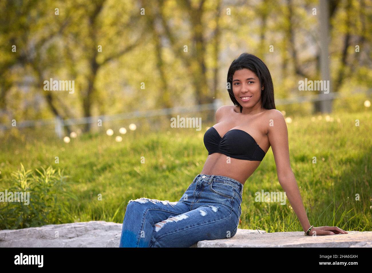 Donna colombiana sorridente che indossa jeans in denim e top nero all'aperto sotto la calda luce del sole a Toronto, Canada. Foto Stock