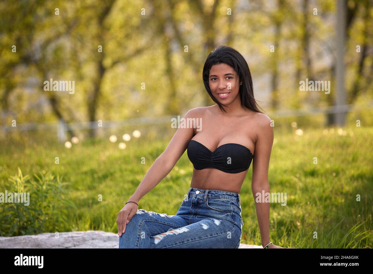 Donna colombiana rilassata con top nero e jeans appoggiati sull'erba in un parco soleggiato a Toronto, Canada. Foto Stock