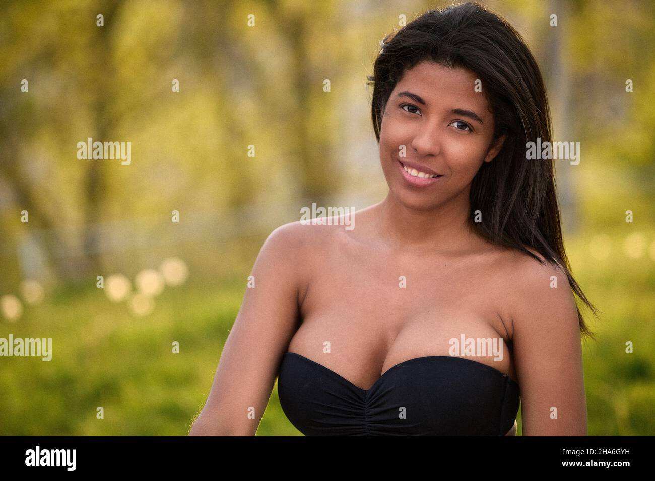 Giovane donna colombiana sorridente con la maglia nera e i jeans in denim all'aperto nel soleggiato parco di Toronto, Canada. Foto Stock