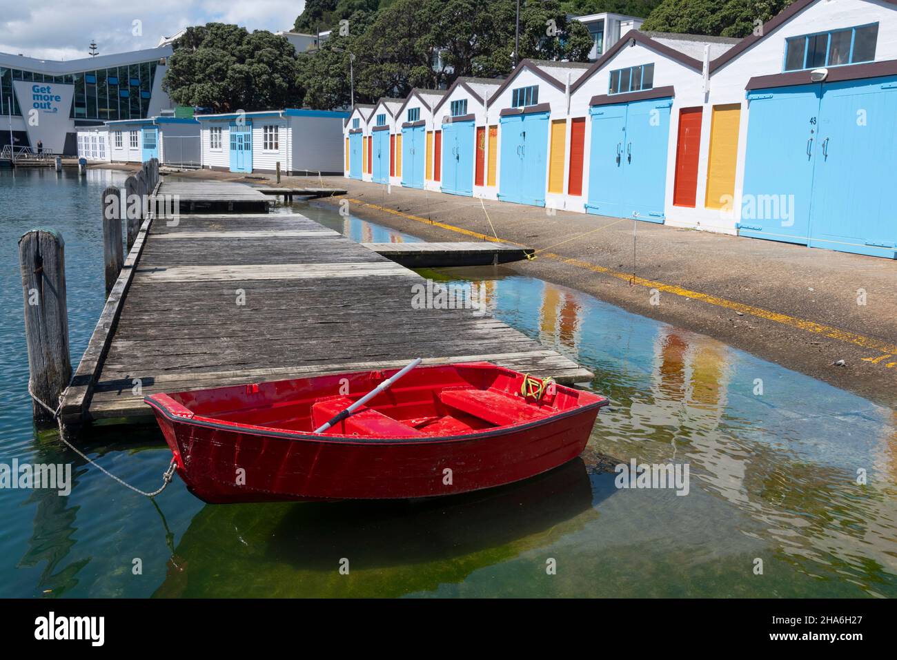 Dingy rosso di fronte a Blue boat sheds, Boat Harbor, Wellington, Isola del Nord, Nuova Zelanda Foto Stock