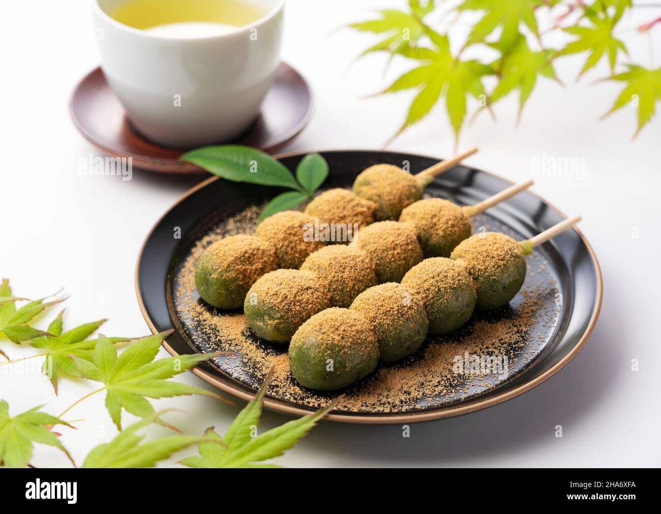 gnocchi di riso al gusto di mugwort ricoperti di farina di soia e tè verde serviti su un piatto nero su sfondo bianco. Gnocchi giapponesi. Foto Stock