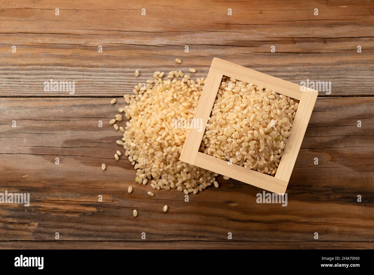 Rosolare il riso in una scatola di legno posta su sfondo di legno. Un mucchio di riso marrone. Composizione vista dall'alto. Foto Stock