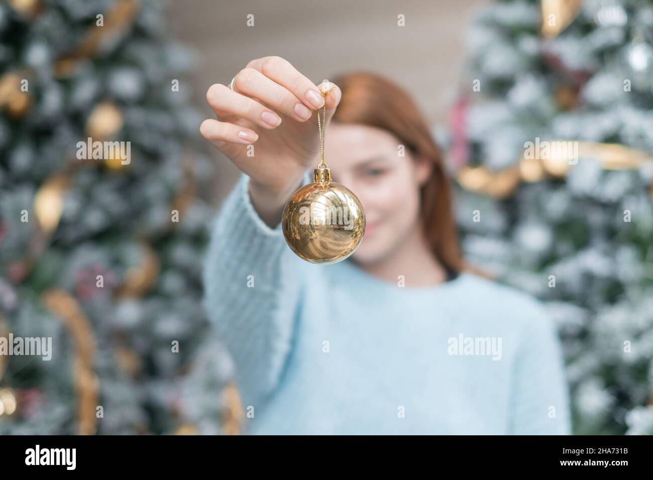 Giovane donna in lana accogliente caldo azzurro maglione tenendo una palla d'oro per decorazione albero di natale. Primo piano foto di oro palla di Natale. Sfocato Foto Stock