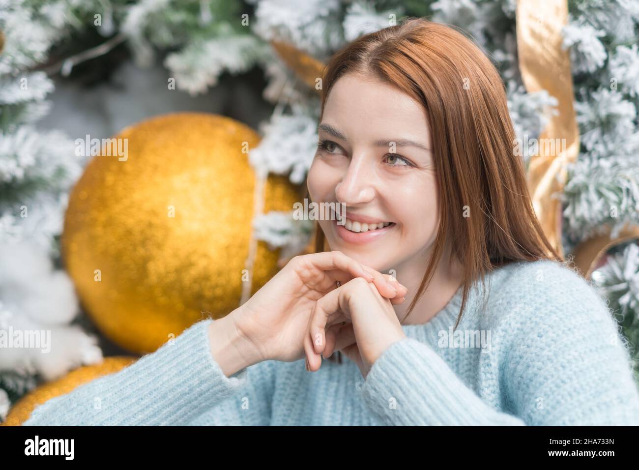 Capodanno primo piano ritratto di bella ragazza caucasica sorridente in lana accogliente caldo azzurro maglione. Albero di Natale sullo sfondo. Foto Stock