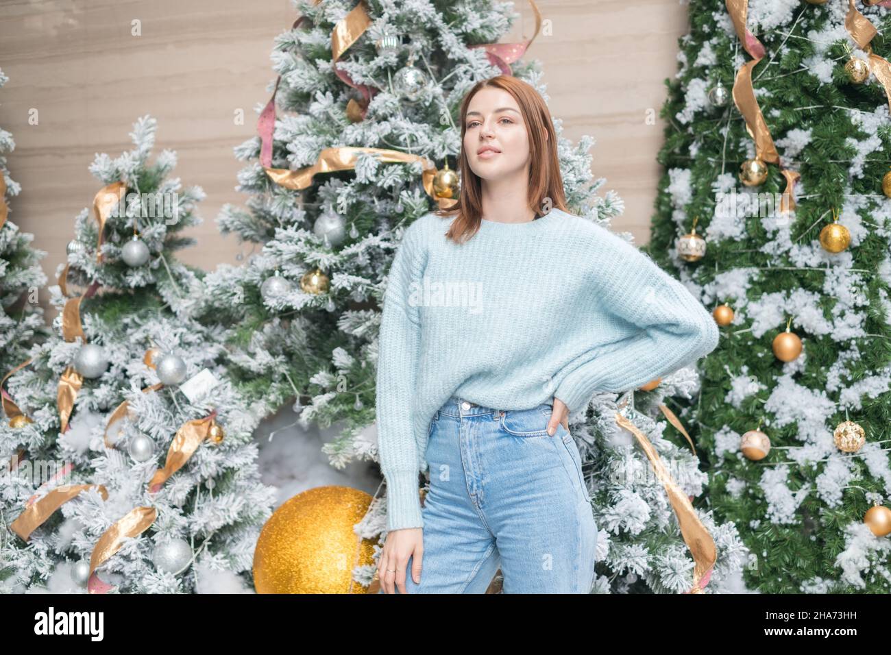 Ritratto di Capodanno della bella giovane donna caucasica in lana accogliente caldo azzurro maglione. Albero di Natale sullo sfondo. Scatto di Natale Foto Stock