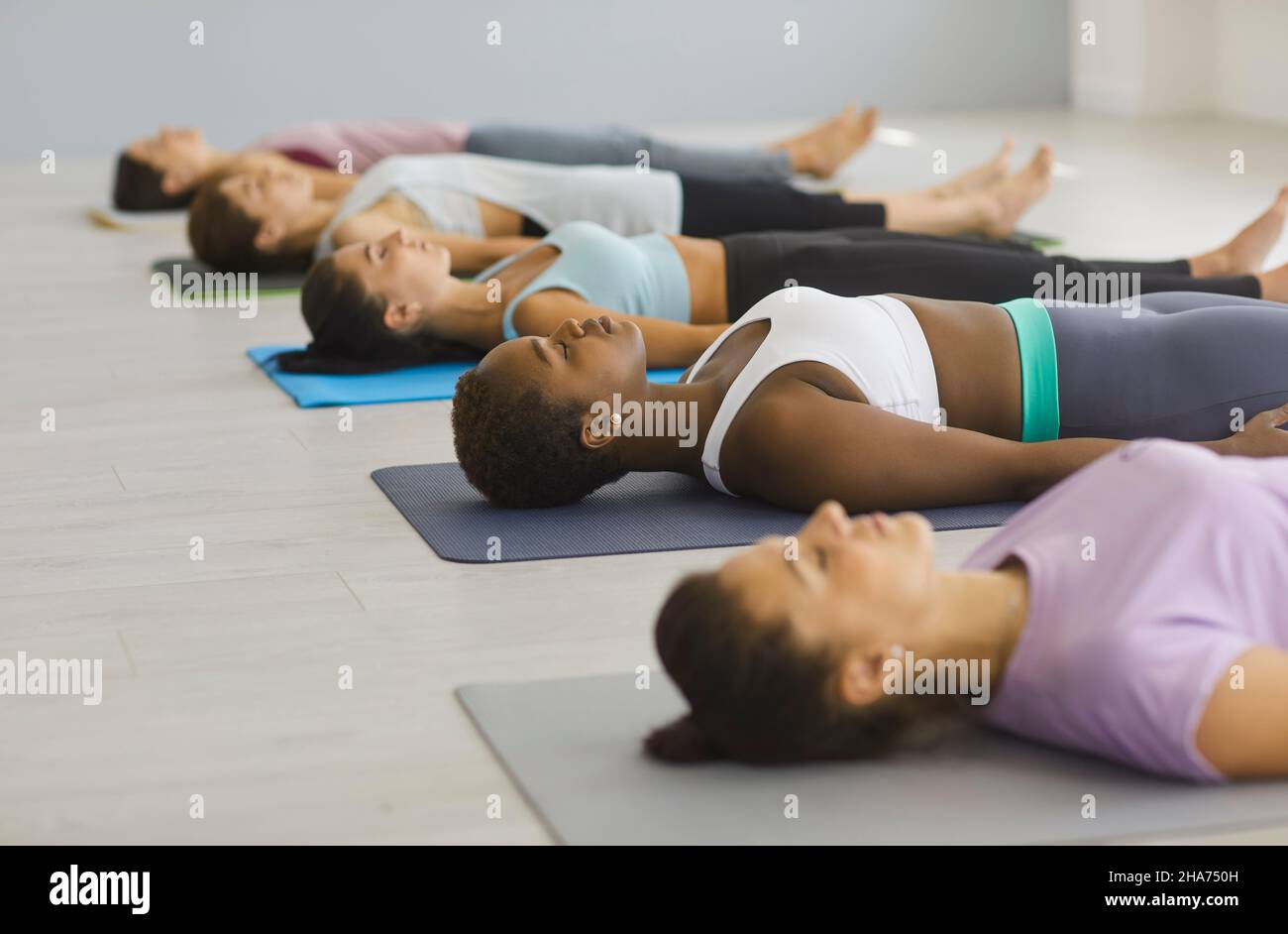 Le giovani donne multirazziali si trovano sul pavimento e praticano esercizi di respirazione profonda in classe yoga. Foto Stock