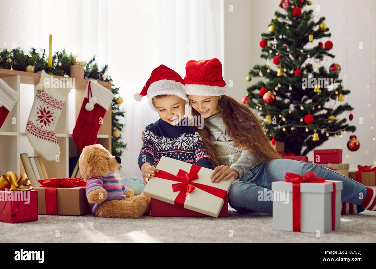 Carino felice ragazzo e ragazza in Babbo Natale cappelli open box con regali di Natale la mattina di festa. Foto Stock